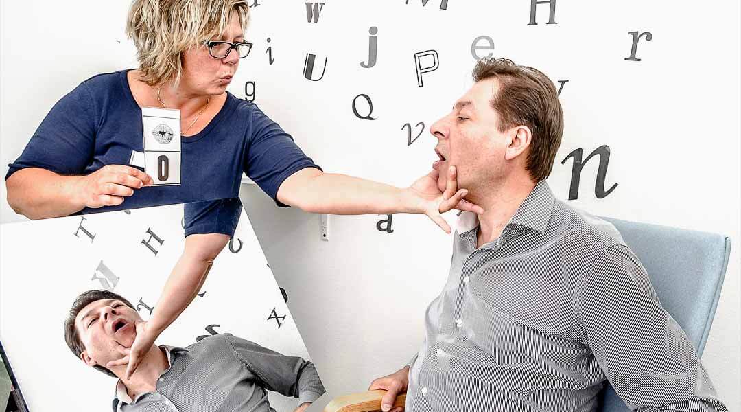 Sprachtherapie Pflegerin übt mit Patient den Buchstaben-O-zu sprechen